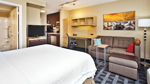 A hotel room with a bed, a desk, a sofa, a TV, and a painting on the wall.