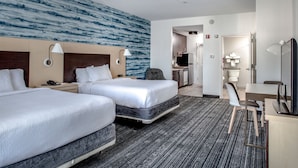 Une chambre d’hôtel avec deux lits, un bureau, une chaise, une télévision et une salle de bain visible à travers une porte ouverte.