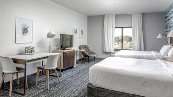 A hotel room with a bed, desk, chairs, and a TV.