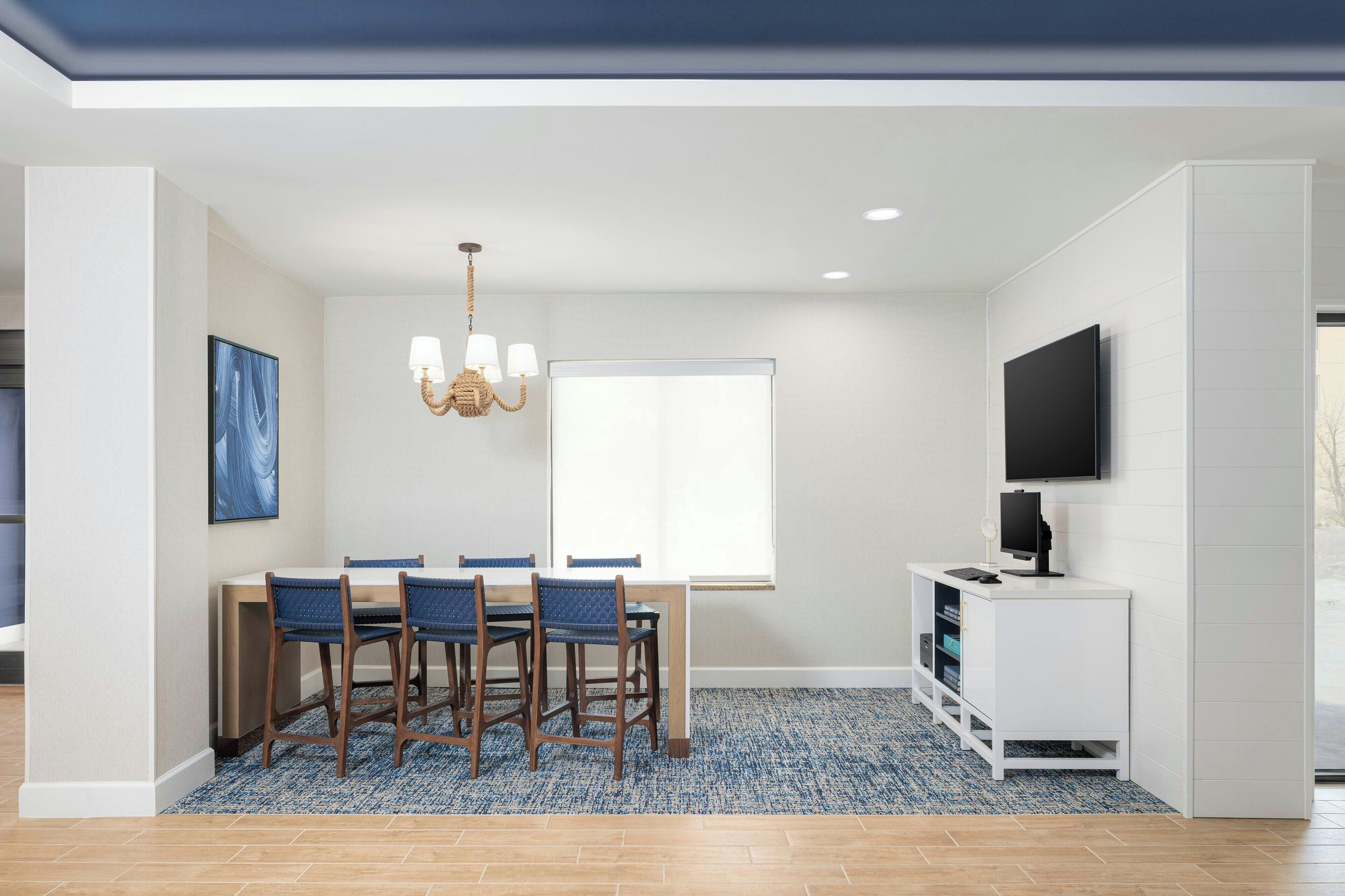 A modern dining area with a chandelier, a flat-screen TV, and a large window.