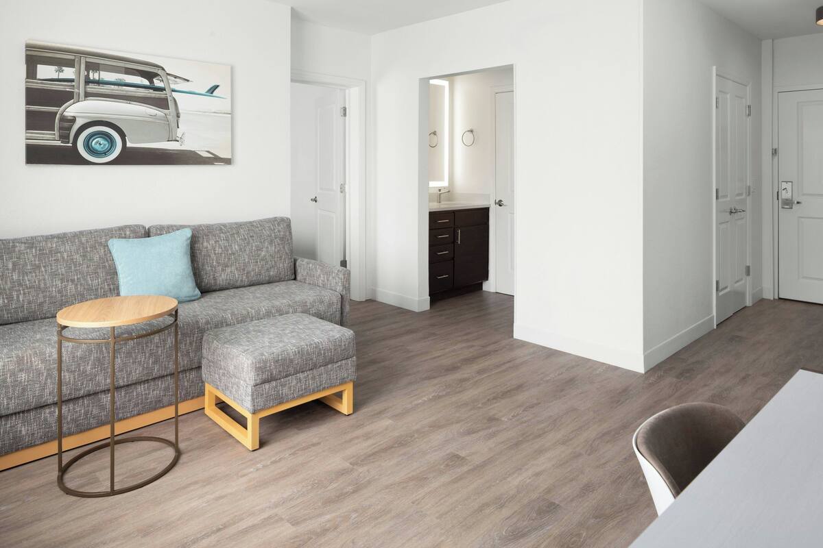 A modern living room with a grey sofa, a round wooden side table, and a dining area with a white table and a brown chair.