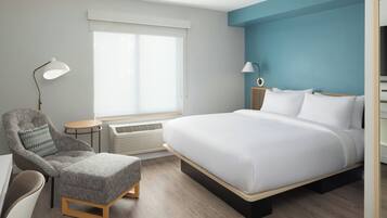 Una moderna camera d'hotel con un letto grande, una poltrona grigia, un piccolo tavolino rotondo e una scrivania.