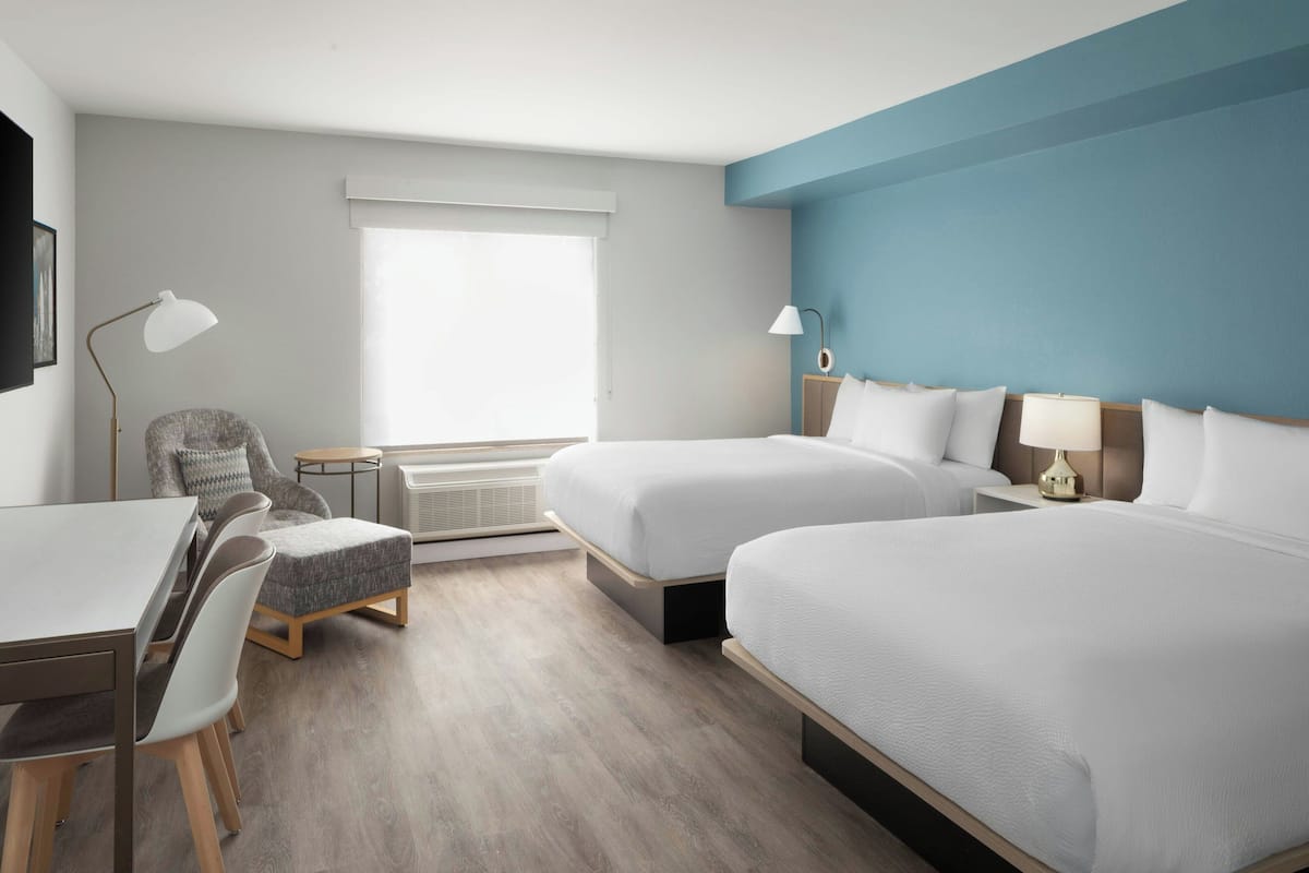 A hotel room with two beds, a desk, a chair, and a window with blinds.