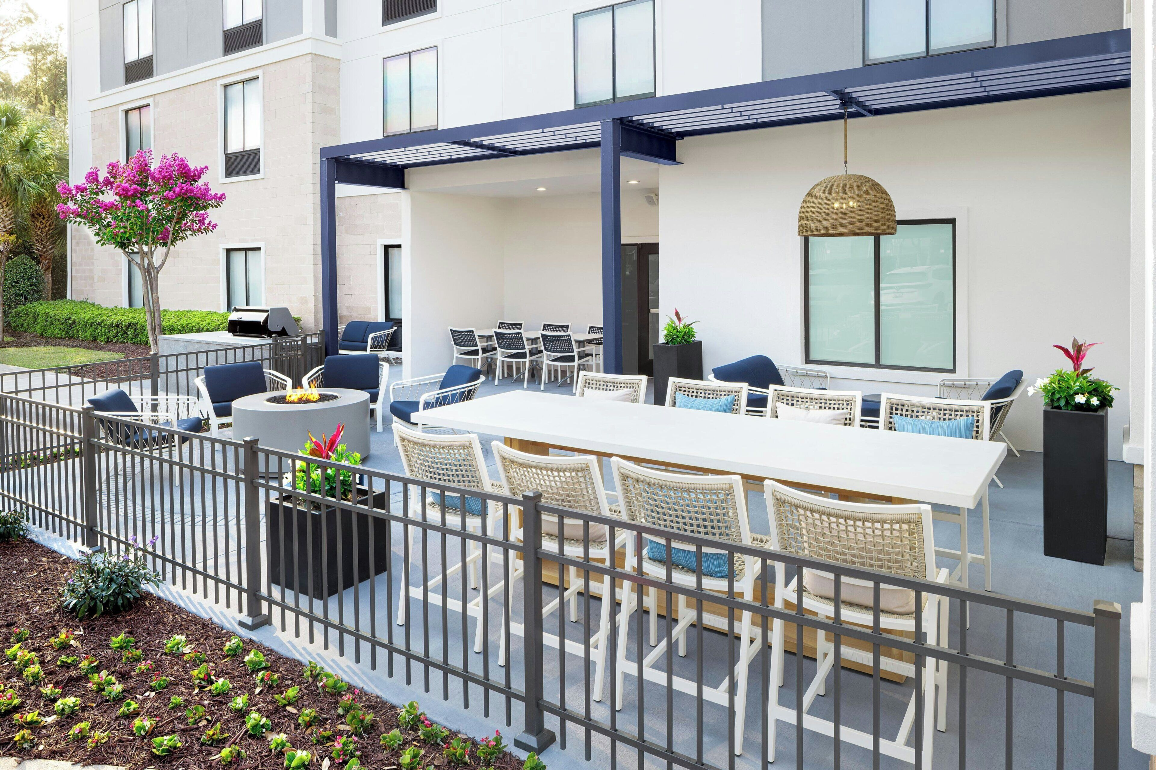 An outdoor patio with a white table and wicker chairs, a grill, and a hanging light fixture.