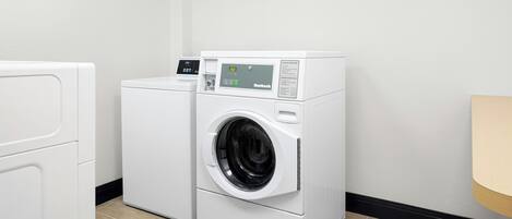 A laundry room with a front-loading washing machine and dryer, a control panel, and a wooden floor.