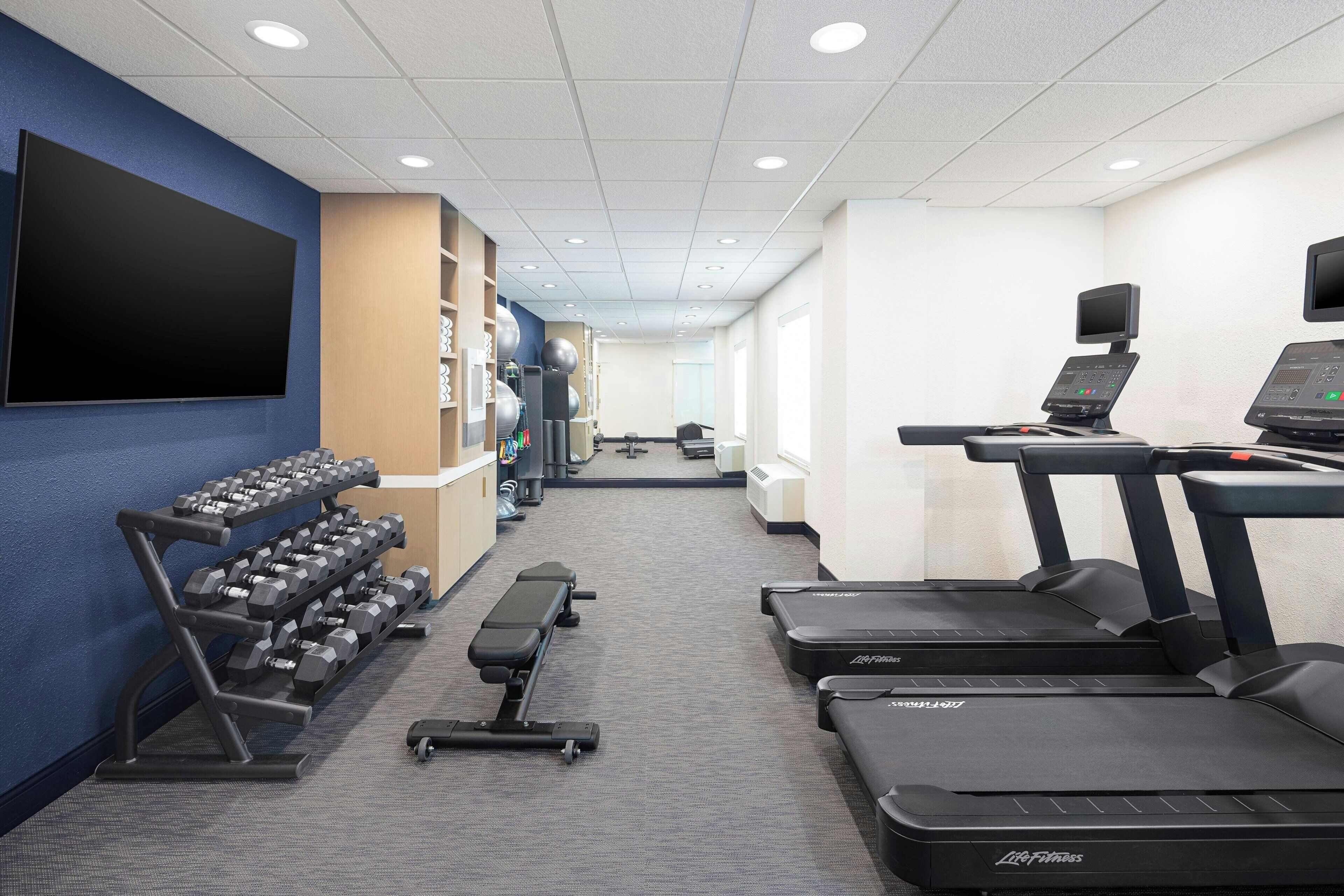 A gym with treadmills, dumbbells, and a TV screen.