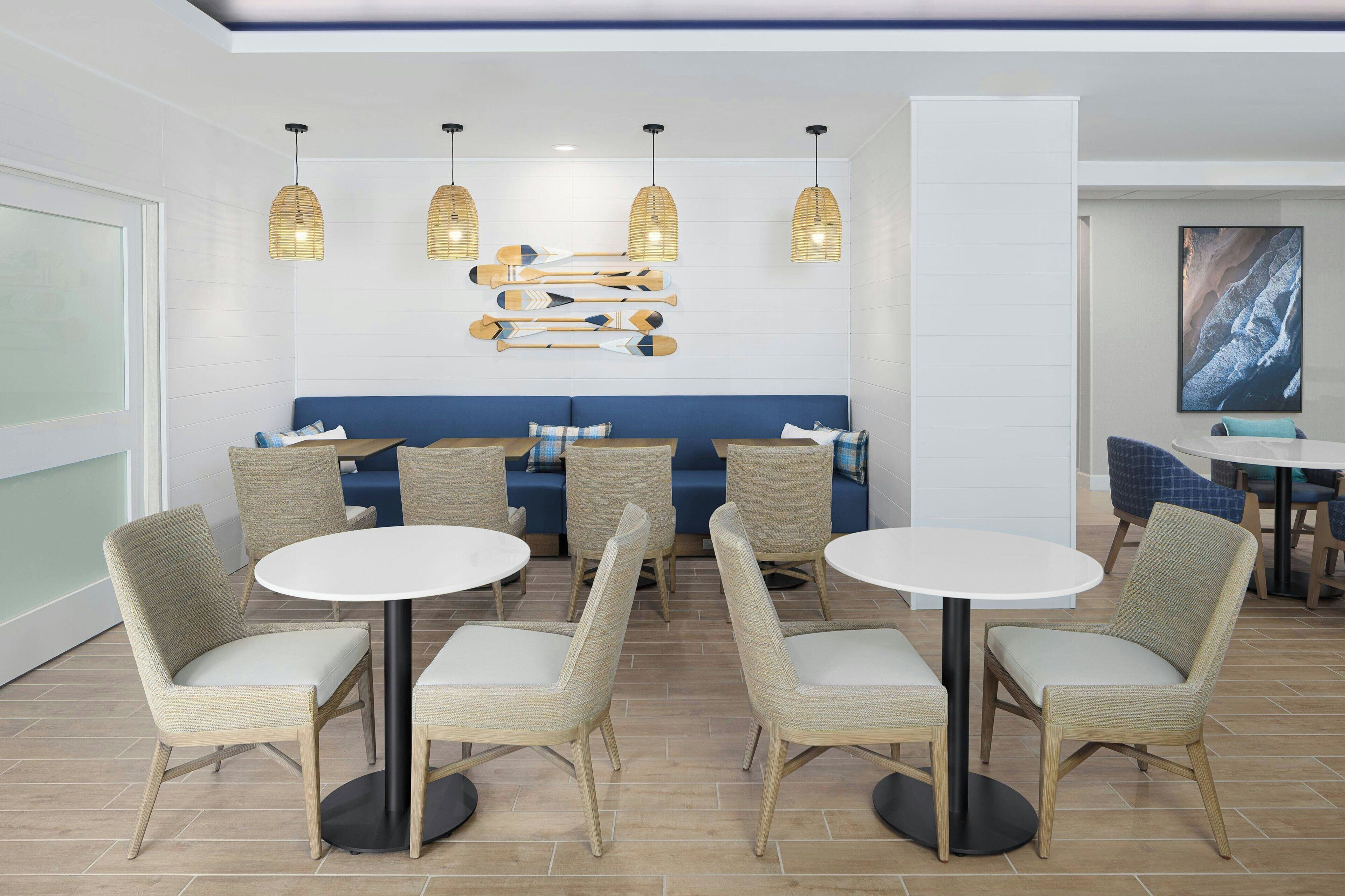 A modern interior with round tables and wicker chairs, a blue sofa, and pendant lighting.