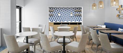 A modern dining area with round tables and chairs, a patterned wall, and pendant lighting.