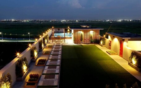 A modern hotel with a rooftop pool, a well-maintained lawn, and a view of the city lights across the water.