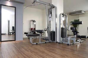 Ein Fitnessraum mit verschiedenen Trainingsgeräten, einem Spiegel und einer Topfpflanze.