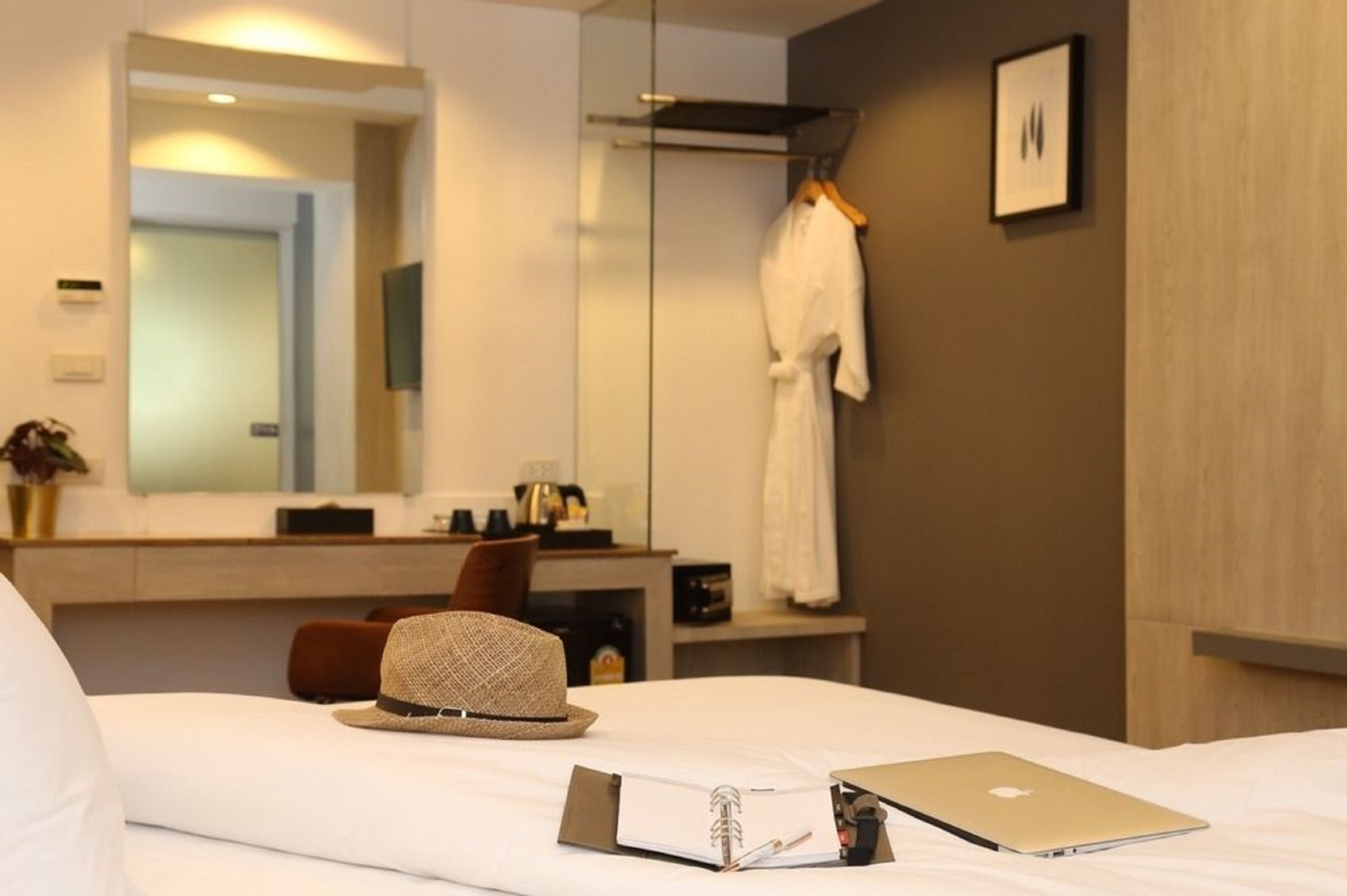 Una habitación de hotel con una cama, una computadora portátil, un sombrero, una bata y un espejo.