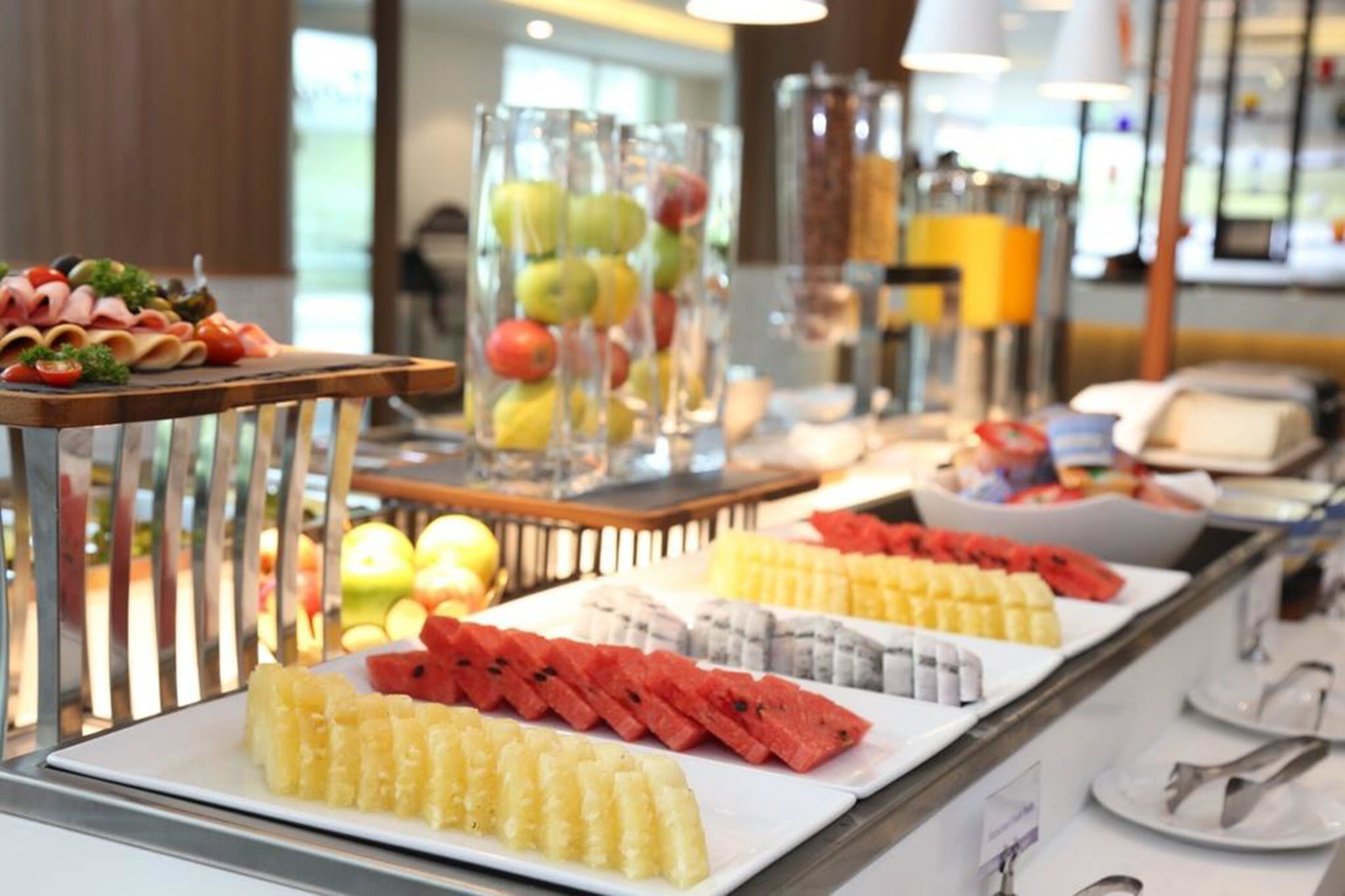 Ein Buffet mit verschiedenen Früchten und Gemüsesorten, darunter Wassermelone, Ananas und Äpfel, ansprechend auf Tellern und in Glasbehältern angerichtet.