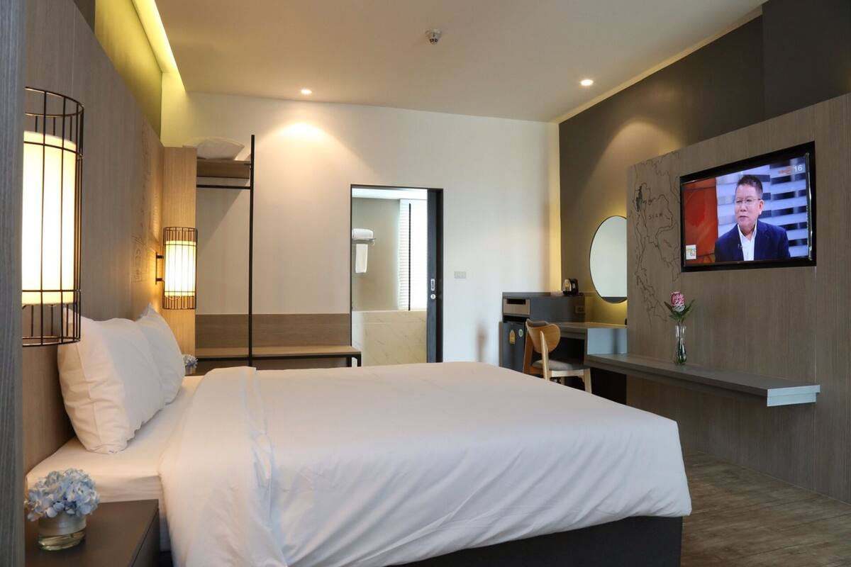 Une chambre d’hôtel moderne avec un grand lit, des lampes de chevet, un bureau, une chaise, une télévision et un miroir au mur.
