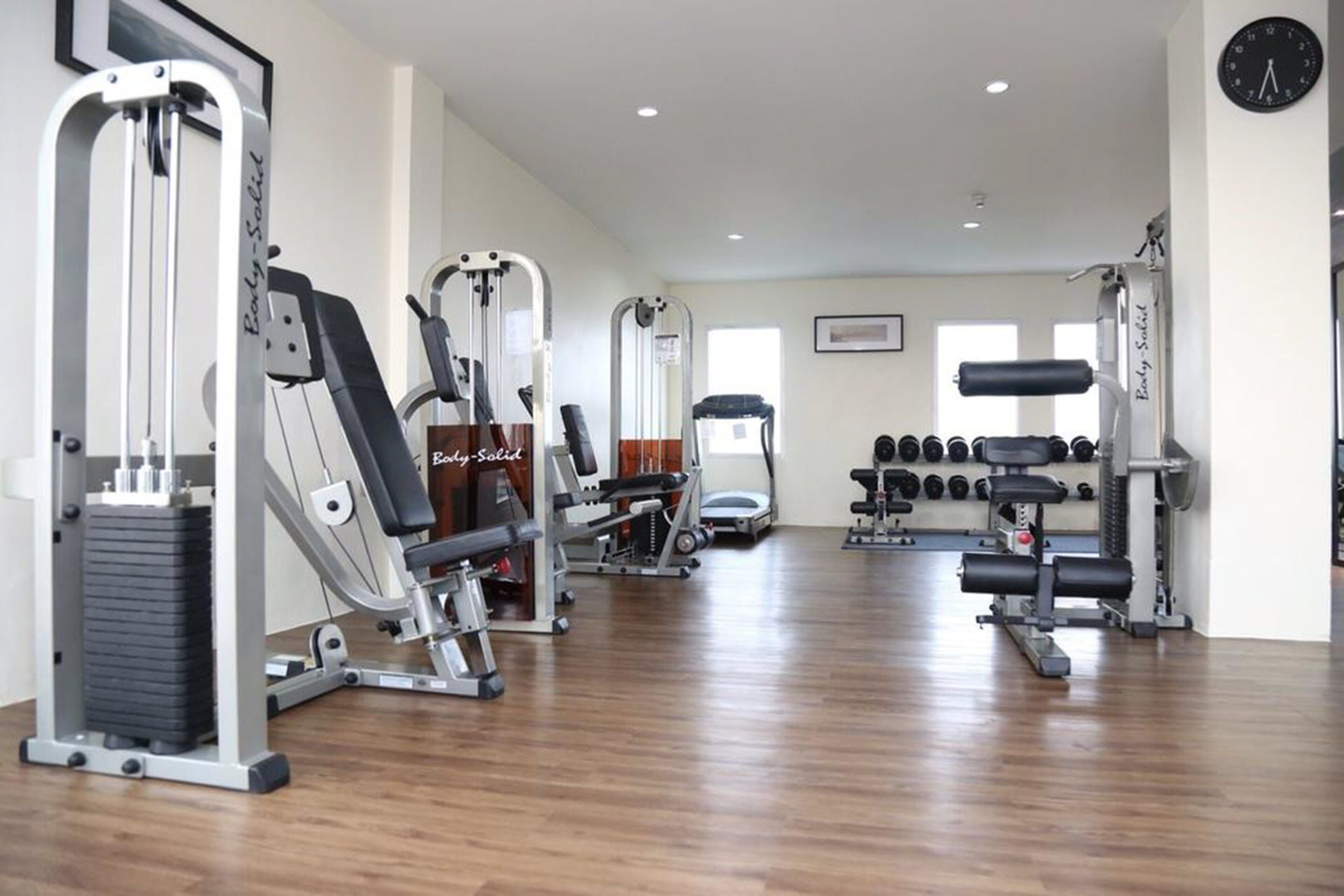 A gym with various exercise machines, dumbbells, and a clock on the wall.