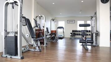 A gym with various exercise machines, dumbbells, and a clock on the wall.