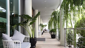Een gang met witte rieten stoelen en potplanten, die uitkomt in een zithoek met uitzicht op het groen.