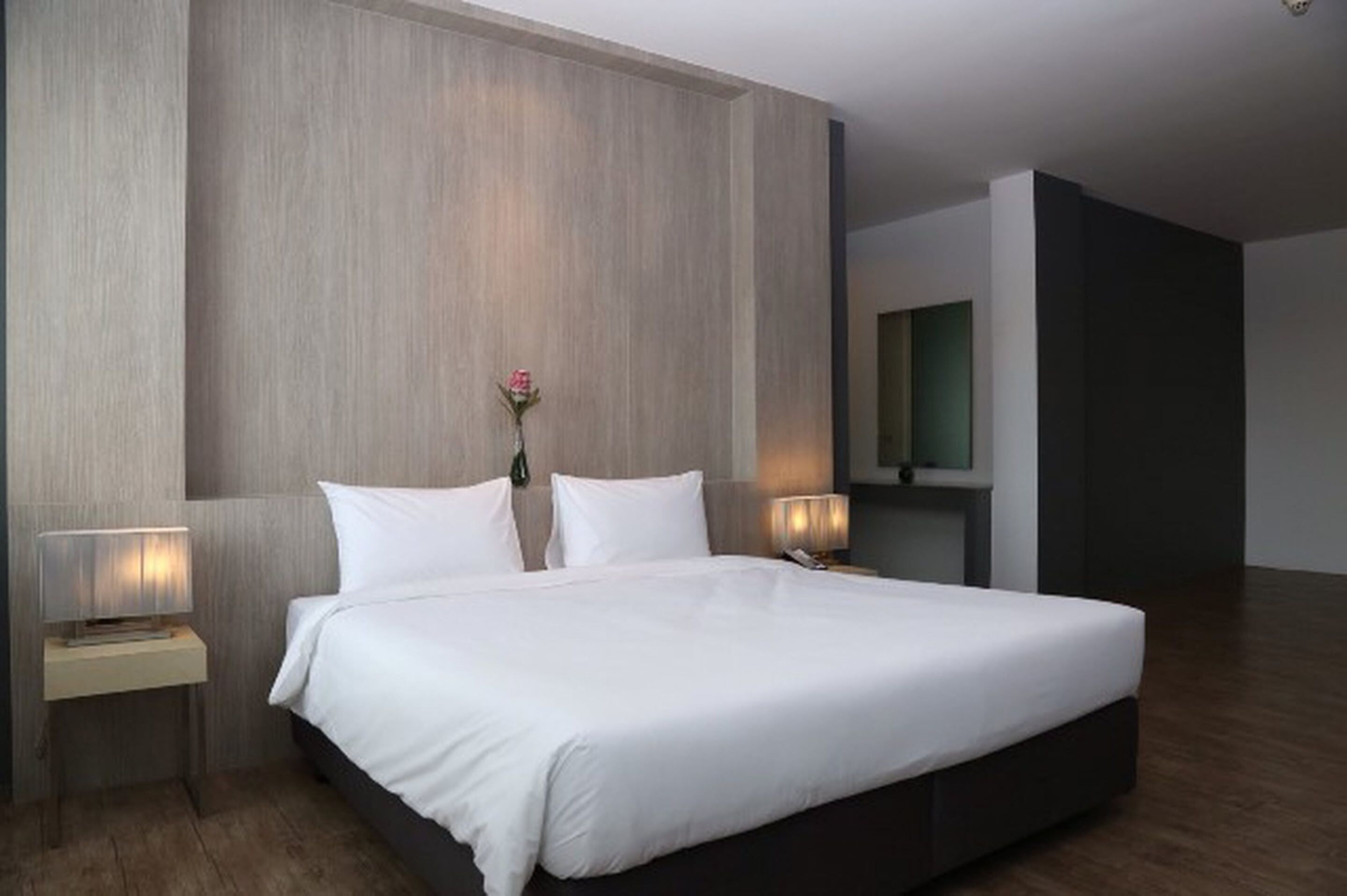 Una habitación de hotel moderna con una cama grande, dos mesitas de noche y un televisor montado en la pared.