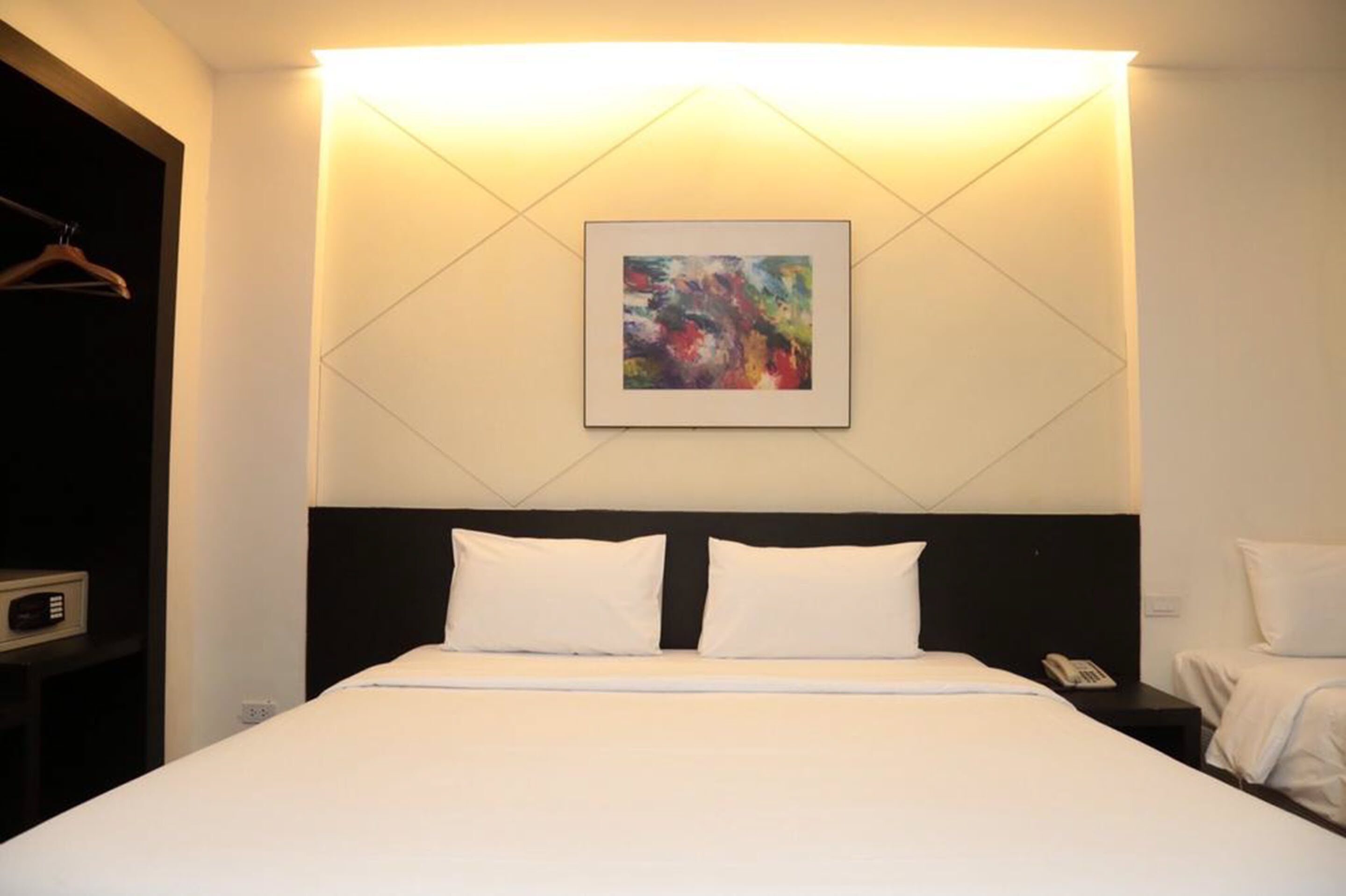 A hotel room with a bed, a bedside table with a phone, and a wall-mounted painting.