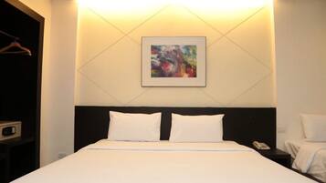 A hotel room with a bed, a bedside table with a phone, and a wall-mounted painting.