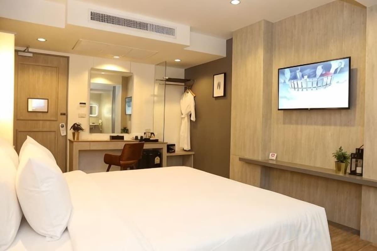 Una habitación de hotel con cama, escritorio, silla, televisión y espejo.