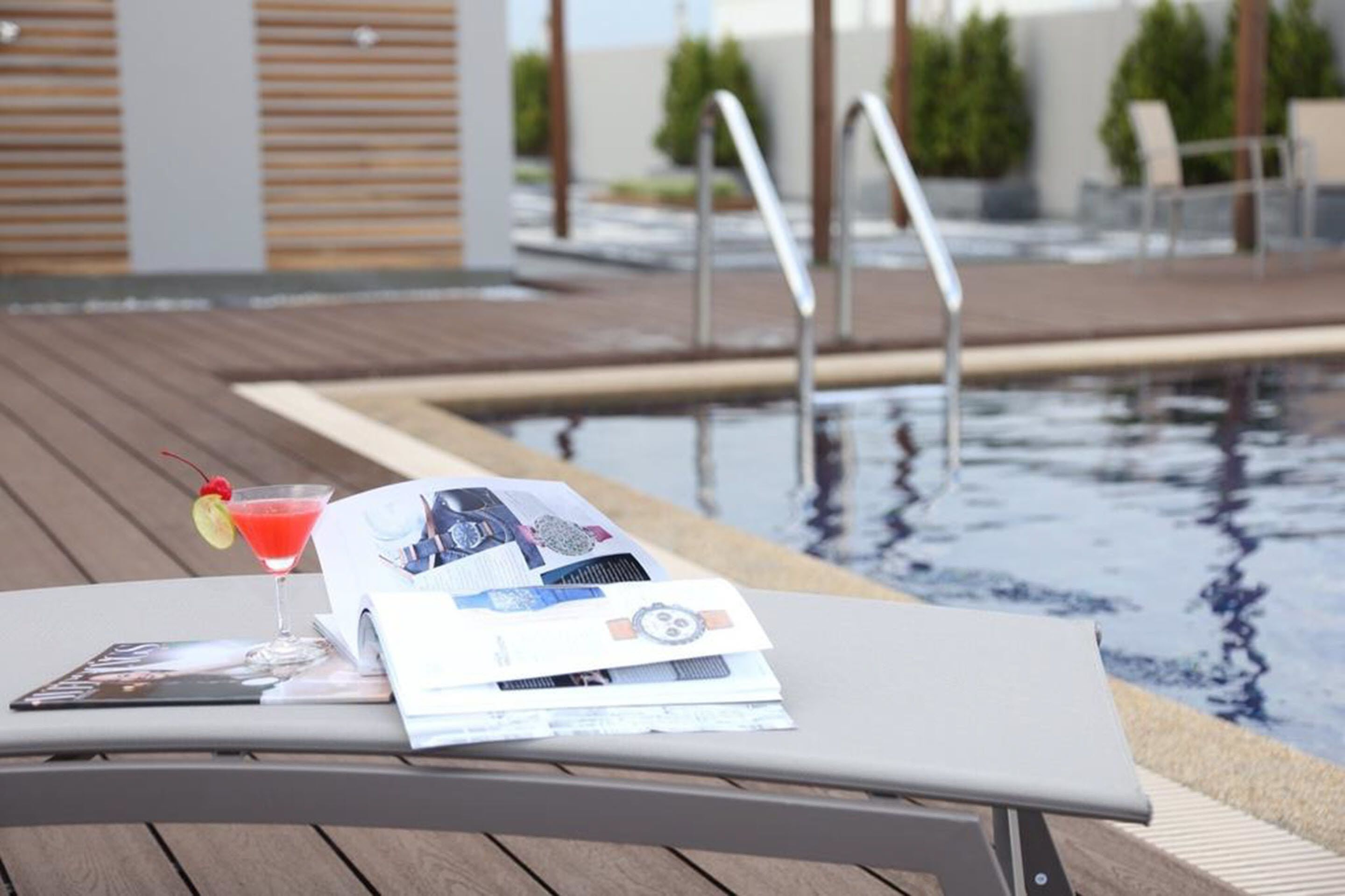 A poolside lounge area with a table, a drink, and magazines.