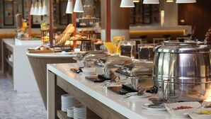 Een buffetopstelling met diverse bakken en bestek, een toonbank met kassa en hangende吊り下げ型照明.