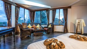 Una habitación amplia con una cama grande, dos sillones, una mesita y vistas a árboles a través de amplios ventanales.