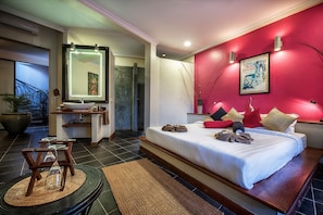 Una habitación de hotel moderna con una cama grande, un baño con espejo y lavamanos, y una pared de acento roja.