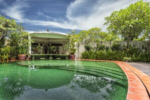 Una piscina de borde curvo, rodeada de exuberante follaje y un área de descanso techada.