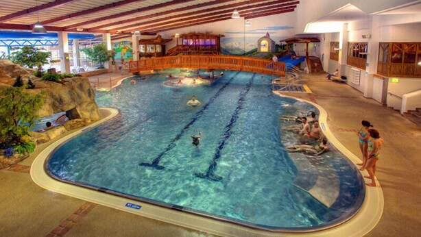 An indoor swimming pool with multiple lanes, wooden deck, and surrounding rock formations. - GB Gondelblick (Soelden)