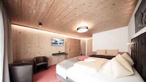 A bedroom with a wooden ceiling, a bed with pillows, a chair, a small table, and a picture on the wall. - GB Gondelblick (Soelden)