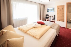 Une chambre d’hôtel avec un lit, deux chaises, une petite table, un téléviseur et un panneau en bois au mur.