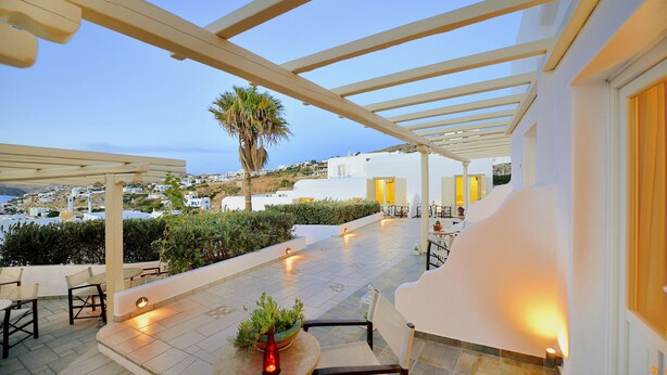 An outdoor patio with seating, a table with a plant, and a view of a coastal town. - Hotel Pelican (Mykonos)