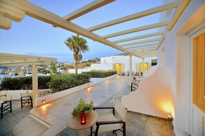 An outdoor patio with seating, a table with a plant, and a view of a coastal town. - Hotel Pelican (Mykonos)