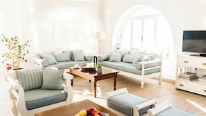 A bright living room with a sofa set, a coffee table, and a TV stand. - Hotel Pelican (Mykonos)