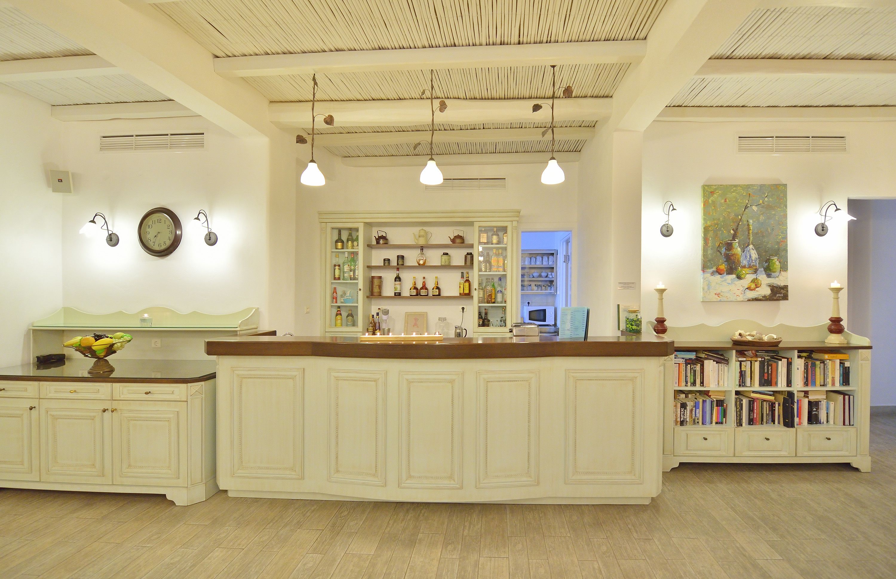 Una cocina con una isla central, armarios blancos y una estantería llena de libros.