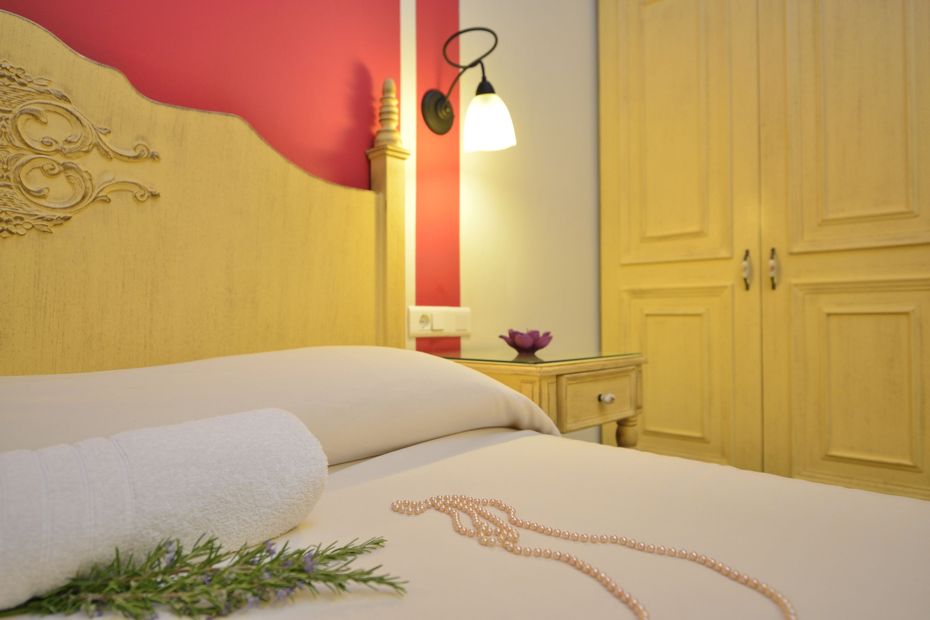 A neatly made bed with a white pillow and a rolled white towel, a bedside table with a lamp, and a wooden wardrobe.