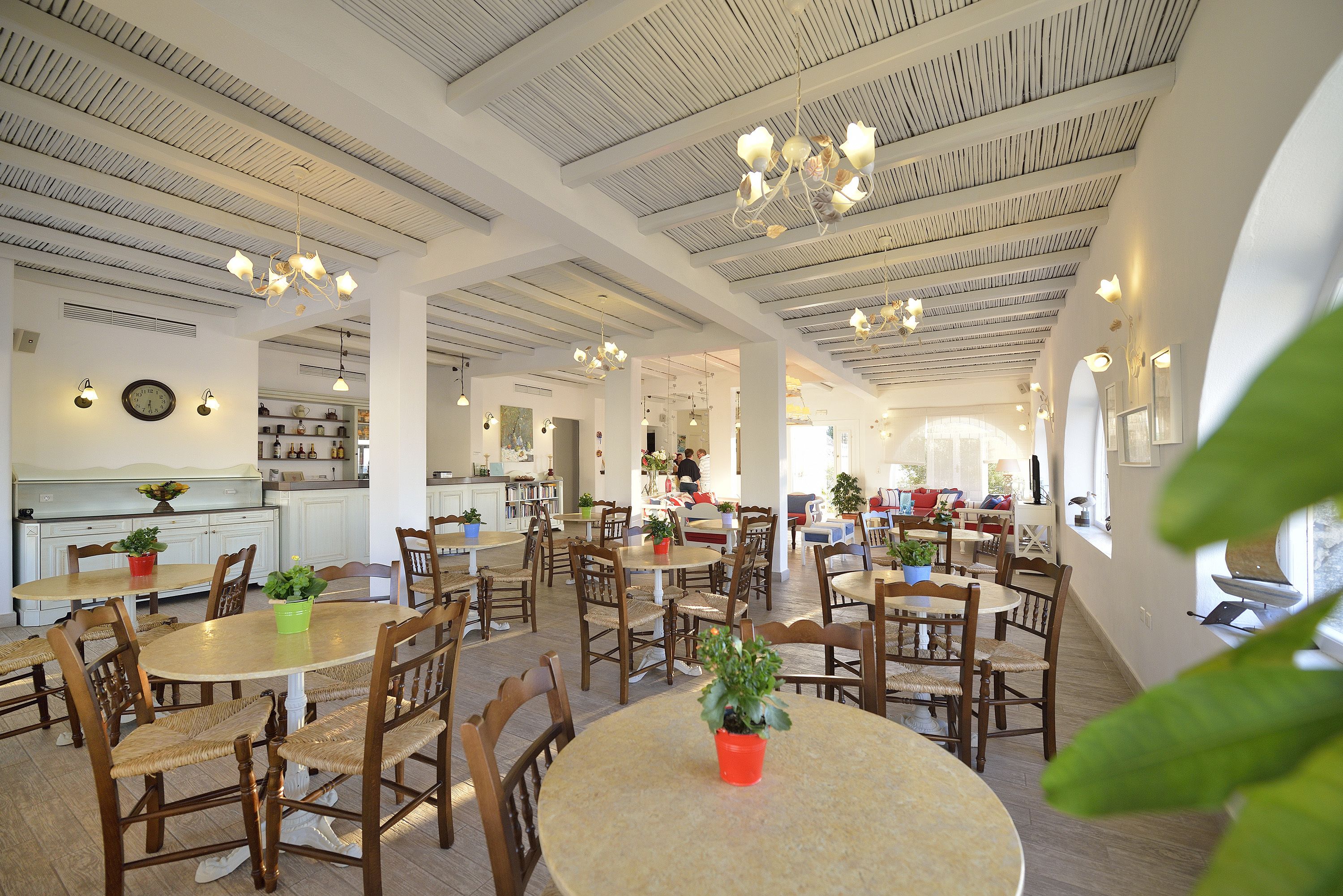 Un vaste espace dédié à la salle à manger, avec plusieurs tables rondes et des chaises en bois, agrémenté de ventilateurs de plafond et de luminaires suspendus.