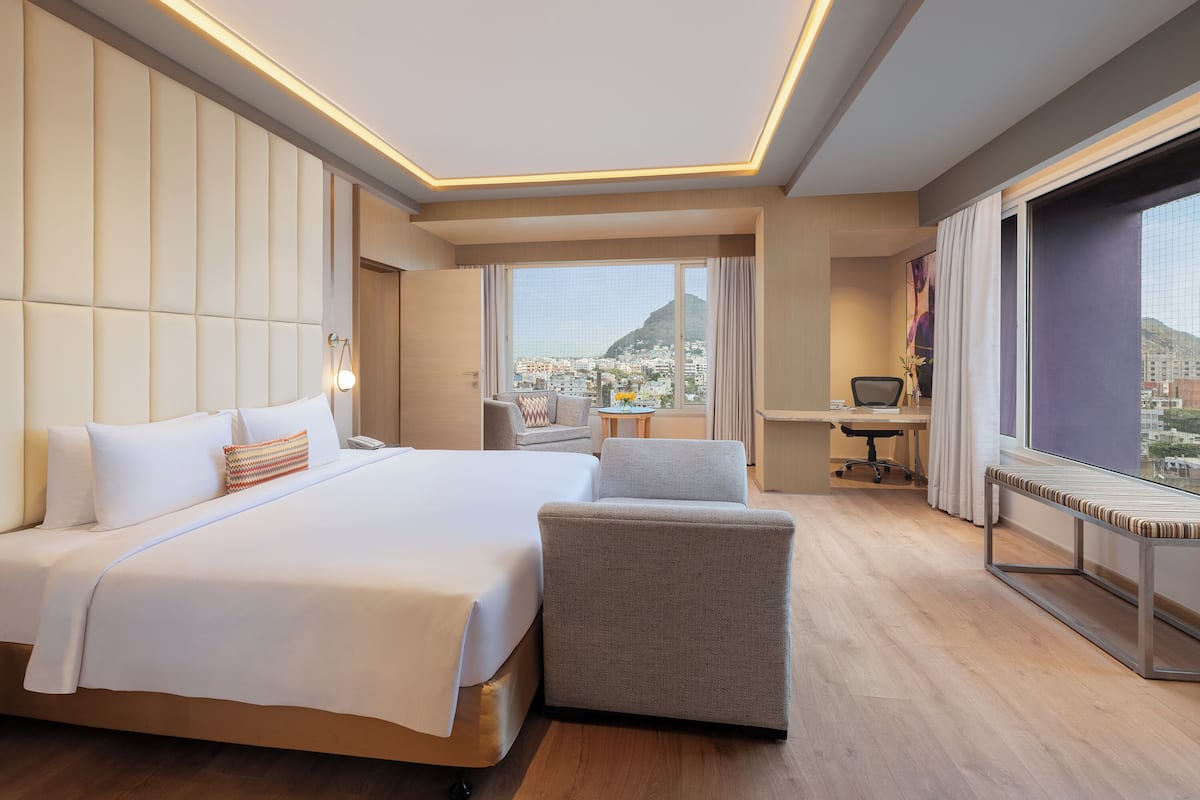 Een hotelkamer met een groot bed, een bureau, een stoel en uitzicht op de stad.