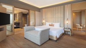 Ein modernes Hotelzimmer mit einem großen Bett, einer Sitzecke, einem Schreibtisch und einem Fernseher.