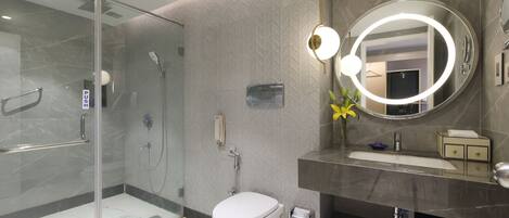Un baño moderno con cabina de ducha de vidrio, inodoro, lavamanos con tocador y un espejo grande con luz circular.