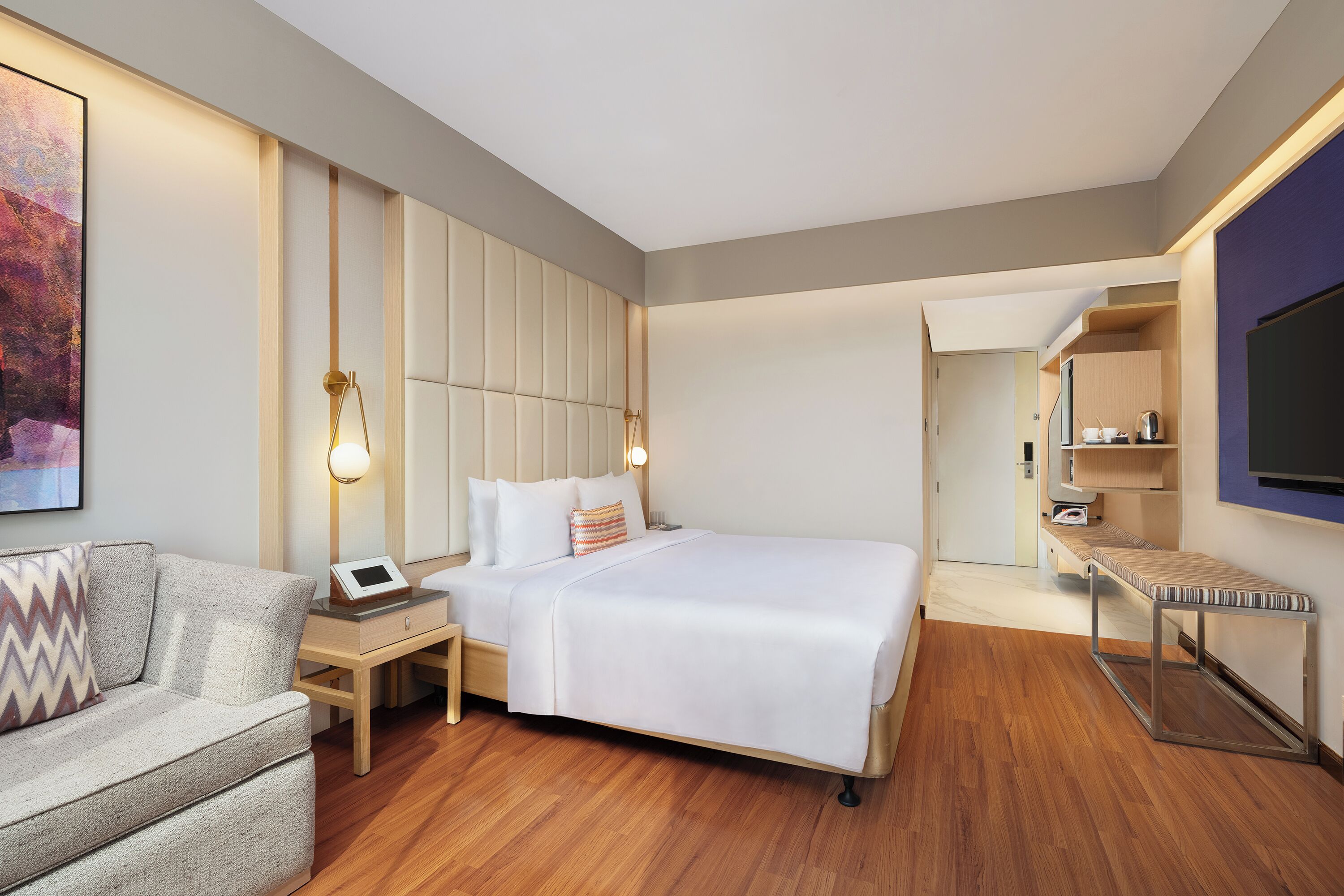Una habitación de hotel moderna con una cama, mesita de noche, lámpara y un televisor fijado a la pared.