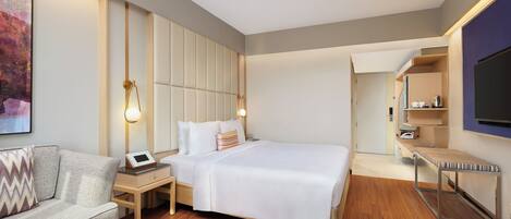 Una habitación de hotel moderna con una cama, mesita de noche, lámpara y un televisor fijado a la pared.