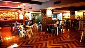 Ein Restaurant mit Fischgrätparkett, weißen und grünen Stühlen sowie einer Bar mit roter Wand.