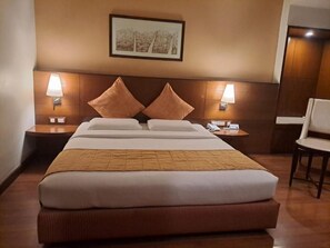 Una camera d'albergo con un letto grande, due lampade sui comodini, un quadro appeso e una sedia.