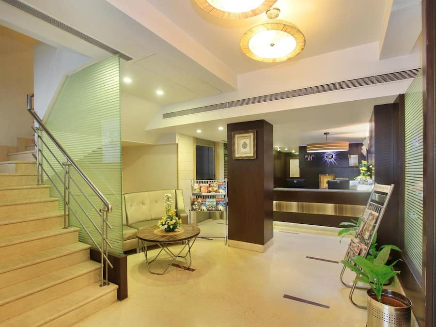 A hotel lobby with a staircase, a reception desk, and a seating area with a table and chairs.