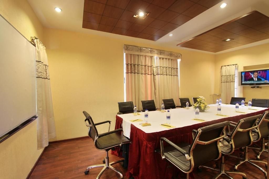 Un salón de conferencias con una larga mesa, sillas, una pantalla de televisión y una pizarra.