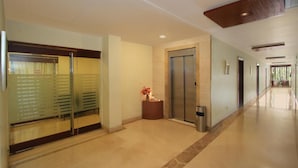 Eine moderne Hotellobby mit Glastür, Empfangsschalter, einem Aufzug und einem Gang zu weiteren Zimmern.