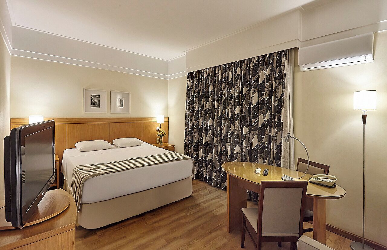 Una habitación de hotel con cama, escritorio, silla, televisor y lámpara.