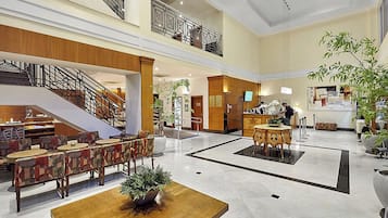 A hotel lobby with a staircase, seating area, reception desk, and a large potted plant.
